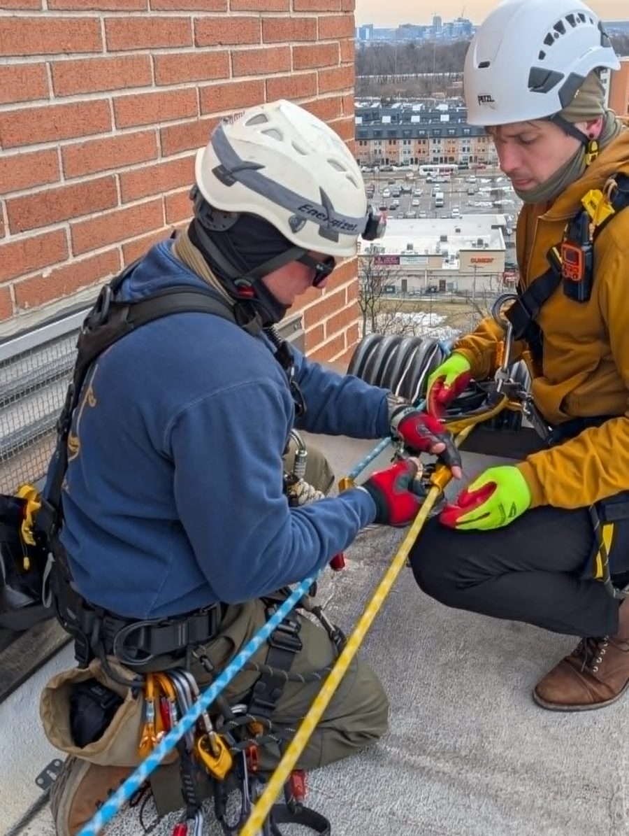 Rope access technicians rigging a descent device on a rooftop